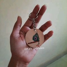 a hand holding a small round keychain with a peacock on it's side