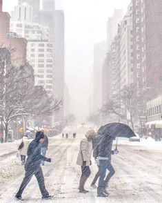 people walking in the snow with umbrellas on a city street near tall buildings and skyscrapers