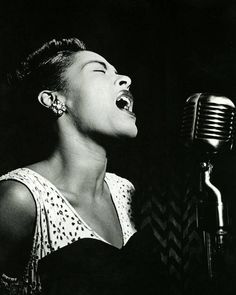 a woman singing into a microphone in front of a black and white photo with her eyes closed