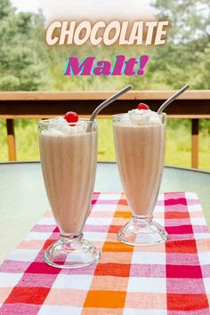 two glasses filled with milkshakes sitting on top of a checkered table cloth