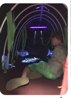 a young boy sitting on the ground in front of a tunnel with fish and plants