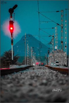 a red traffic light sitting on the side of a train track next to a mountain