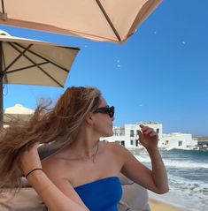 a woman sitting on the beach with her hair blowing in the wind and an umbrella over her head