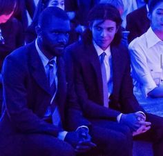 two men sitting next to each other in front of a crowd at a fashion show