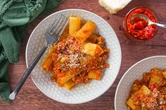 two white plates filled with pasta and sauce on top of a wooden table next to bread