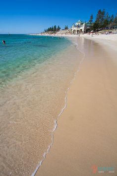 people are swimming in the clear blue water on a beach with white sand and green trees