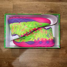 a pair of pink and green shoes in a box on a wooden floor next to a shoelace