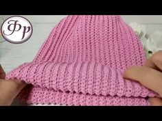 someone crocheting a pink hat on top of a white table next to flowers