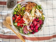 a white bowl filled with salad next to a cup of coffee and spoons on top of a checkered table cloth