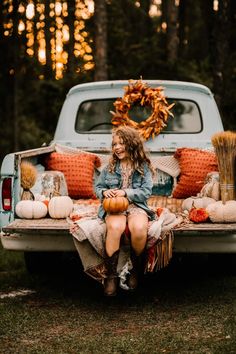 a woman sitting in the back of a pick up truck with pumpkins and hay