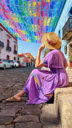 a woman in a purple dress and straw hat sitting on the side of a street