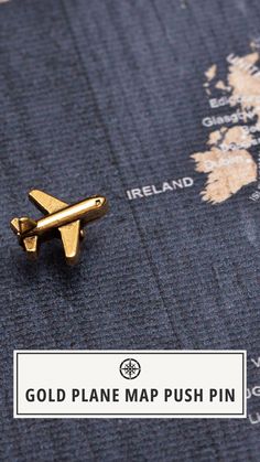 a gold plane map push pin sitting on top of a blue blanket with the words,'gold plane map push pin '