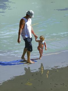 a man and child are walking on the beach with their feet in the water while holding hands