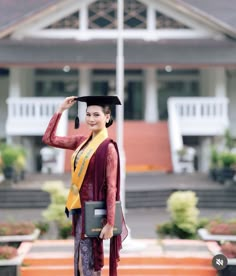 a woman wearing a graduation gown and holding a black hat in front of a building