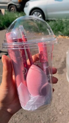 a person holding up a plastic cup with makeup and lipstick in it on the street