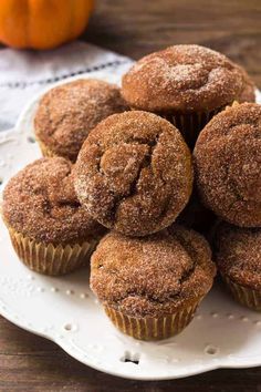 a pile of cinnamon muffins on a white plate next to an orange pumpkin