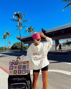 a woman in shorts and a white sweatshirt pulling a suitcase down the street with her hand on her head