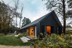 a small black cabin in the middle of some trees and grass, with stairs leading up to it