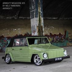 an old green car parked in front of a wall with graffiti on it's walls