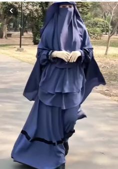 a woman in a blue hijab is walking down the street with her hands on her hips