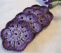 three crocheted coasters sitting on top of a table next to purple flowers