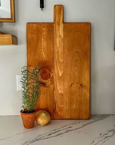 a wooden cutting board sitting on top of a counter next to two potted plants