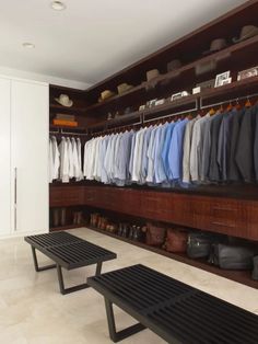 a walk in closet filled with lots of shirts and pants hanging on wooden shelves next to two benches