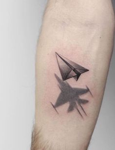 a black and white photo of a paper airplane tattoo on the left forearm, with an arrow in the middle