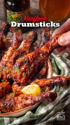 a person holding a piece of chicken in front of a plate with wings and lemons