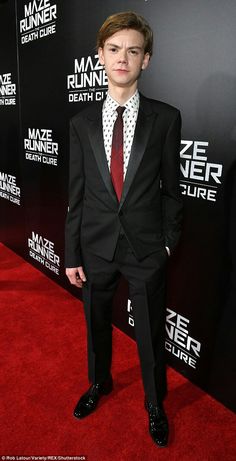 a young man in a suit and tie standing on a red carpet at the maze runner premiere