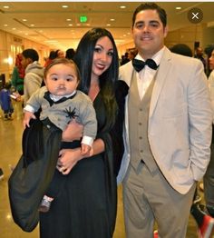 a man and woman in formal wear posing for the camera with a baby dressed as dracula