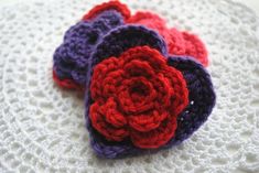 four crocheted flowers laying on top of a white doily with red and purple petals