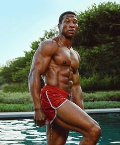 a man standing in front of a swimming pool wearing red swim trunks and no shirt