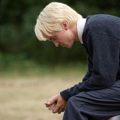 a young man sitting on top of a wooden bench holding his hands together while looking down