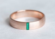 a rose gold wedding band with a green emerald stone in the center, on a white background