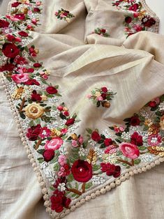 an embroidered table cloth with red flowers and pearls on the edge is laying on a white surface