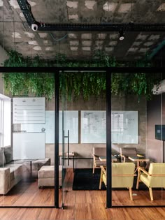 an office with wooden floors and glass walls, plants growing on the ceiling above it