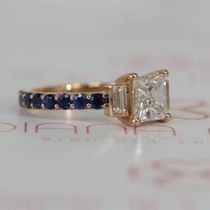 a diamond and blue sapphire ring sitting on top of a piece of paper