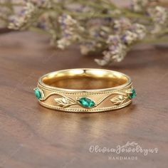 a gold band with green stones and leaves on the side, sitting on a wooden surface