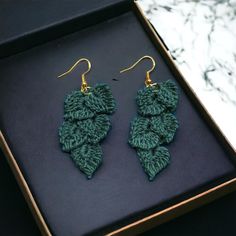 two green crocheted leaves are hanging from gold earwires in a box