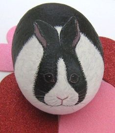 a black and white rabbit painted on top of a red heart shaped object with pink circles around it