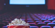 a red cup filled with popcorn sitting on top of a table in front of an empty screen