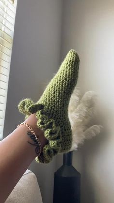 a woman's hand wearing a green crocheted mitt with white feathers