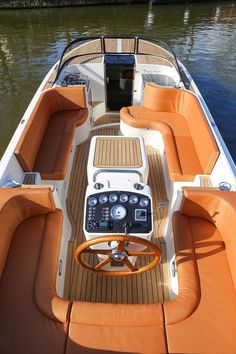 the inside of a boat with orange seats and steering wheel, on water near shore