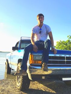 a man sitting on the back of a pick up truck next to a body of water