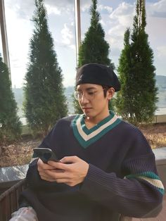 a young man sitting on a bench looking at his cell phone while wearing a hat