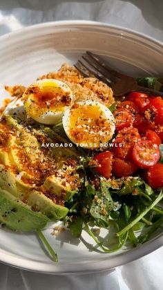 a white plate topped with an egg, tomato and avocado salad next to a fork