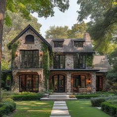 a large stone house surrounded by lush green trees and bushes with steps leading to the front door