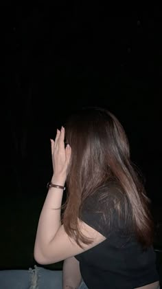 a woman sitting on the ground with her hand up to her face, in front of a dark background