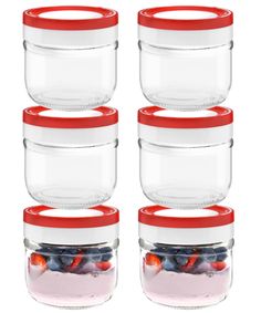 four glass storage containers with red lids are stacked on top of each other and filled with berries